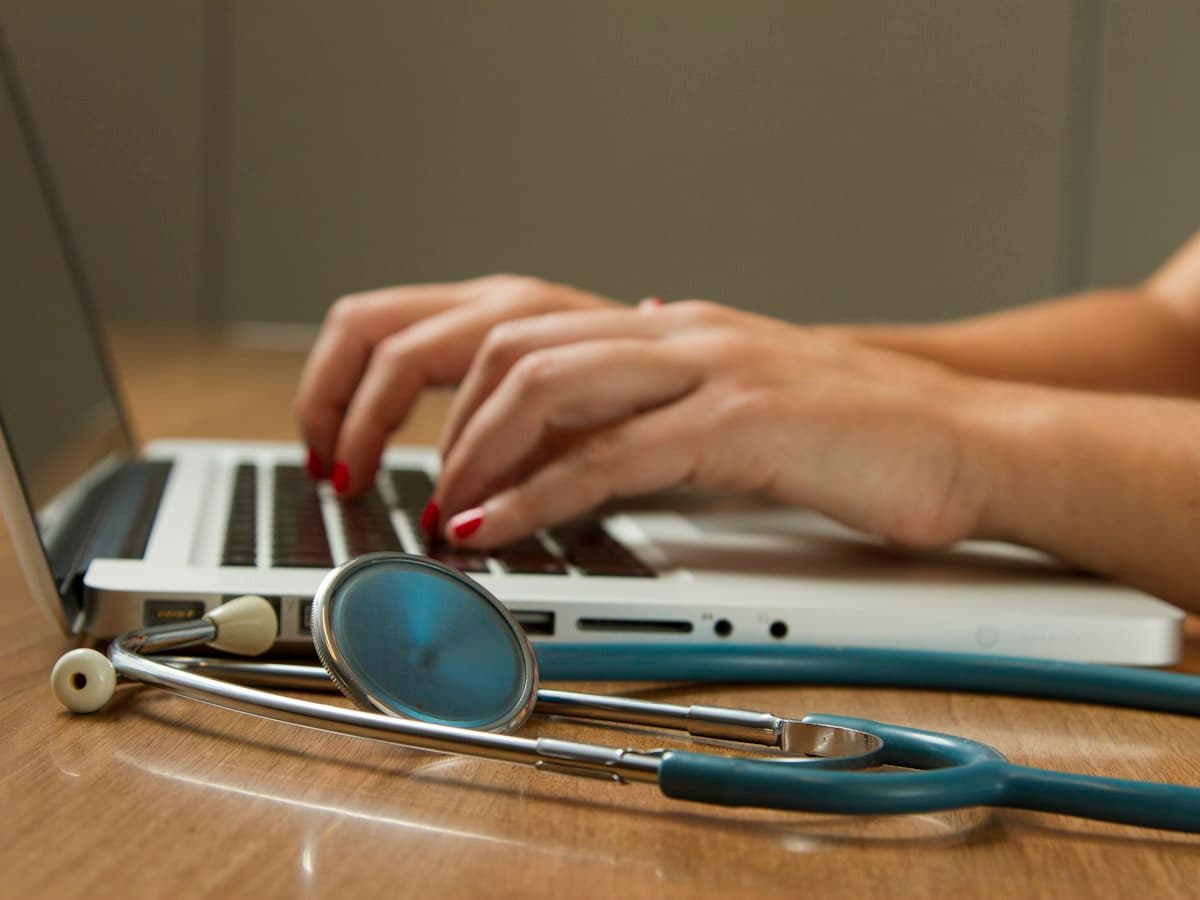 Medical biller entering claims on a laptop beside a stethoscope